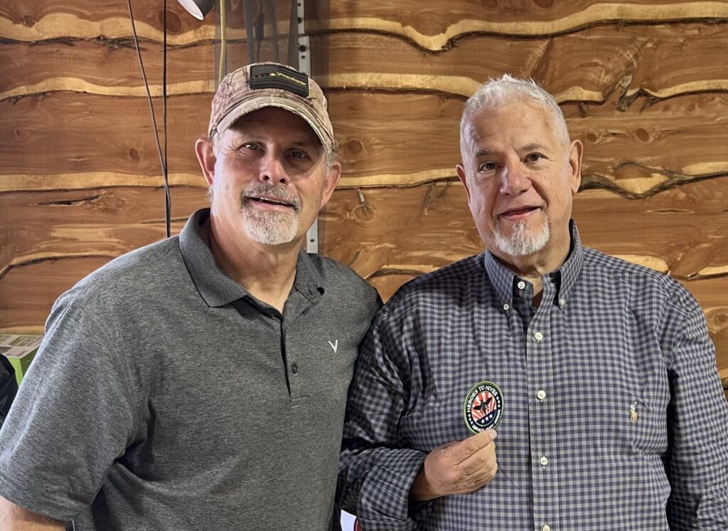 Two men posing together indoors, smiling warmly at the camera.