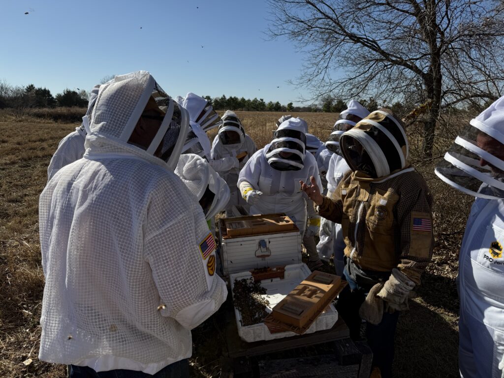 Beekeepers in protective suits tending to bee hives outdoors.